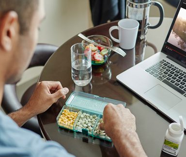 Lifestyle image showing a man sitting at a table with a laptop, Nutrilite Double X, vitamin B, a serving of fruit salad and coffee in a French press. Breakfast provides nutrients we need for energy so we can focus and perform throughout the day.