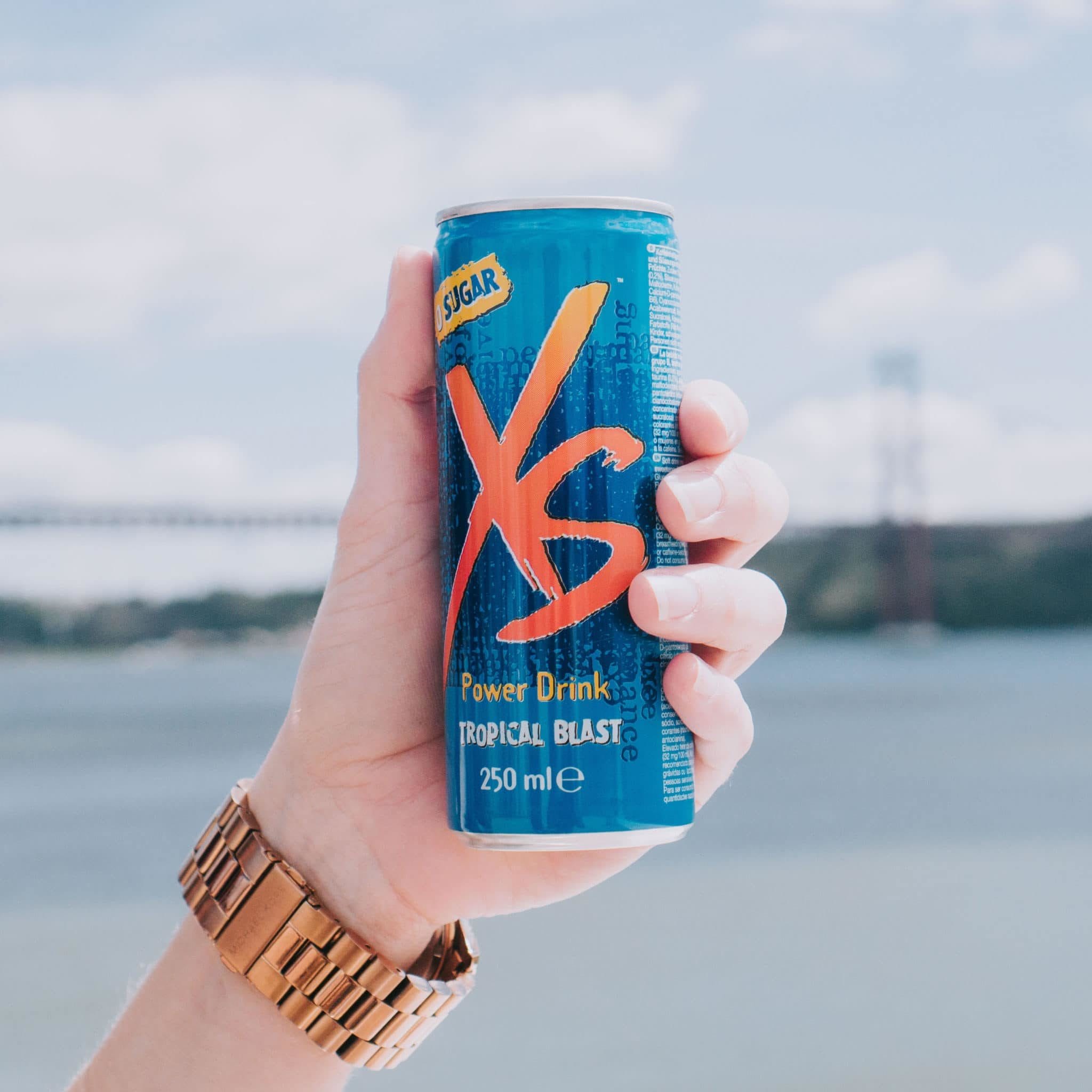 A close up of a hand holding an XS Power Drink with the Golden Gate Bridge in the background. Quench your thirst and improve your body's hydration with XS Energy drinks.