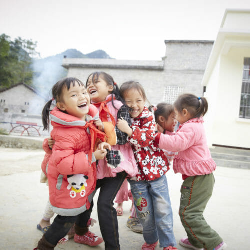 5 smiling and laughing young Chinese girls hugging on a playground