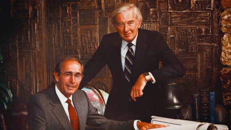 Vintage photo of Rich DeVos and Jay Van Andel posing behind a desk and looking at blueprints.